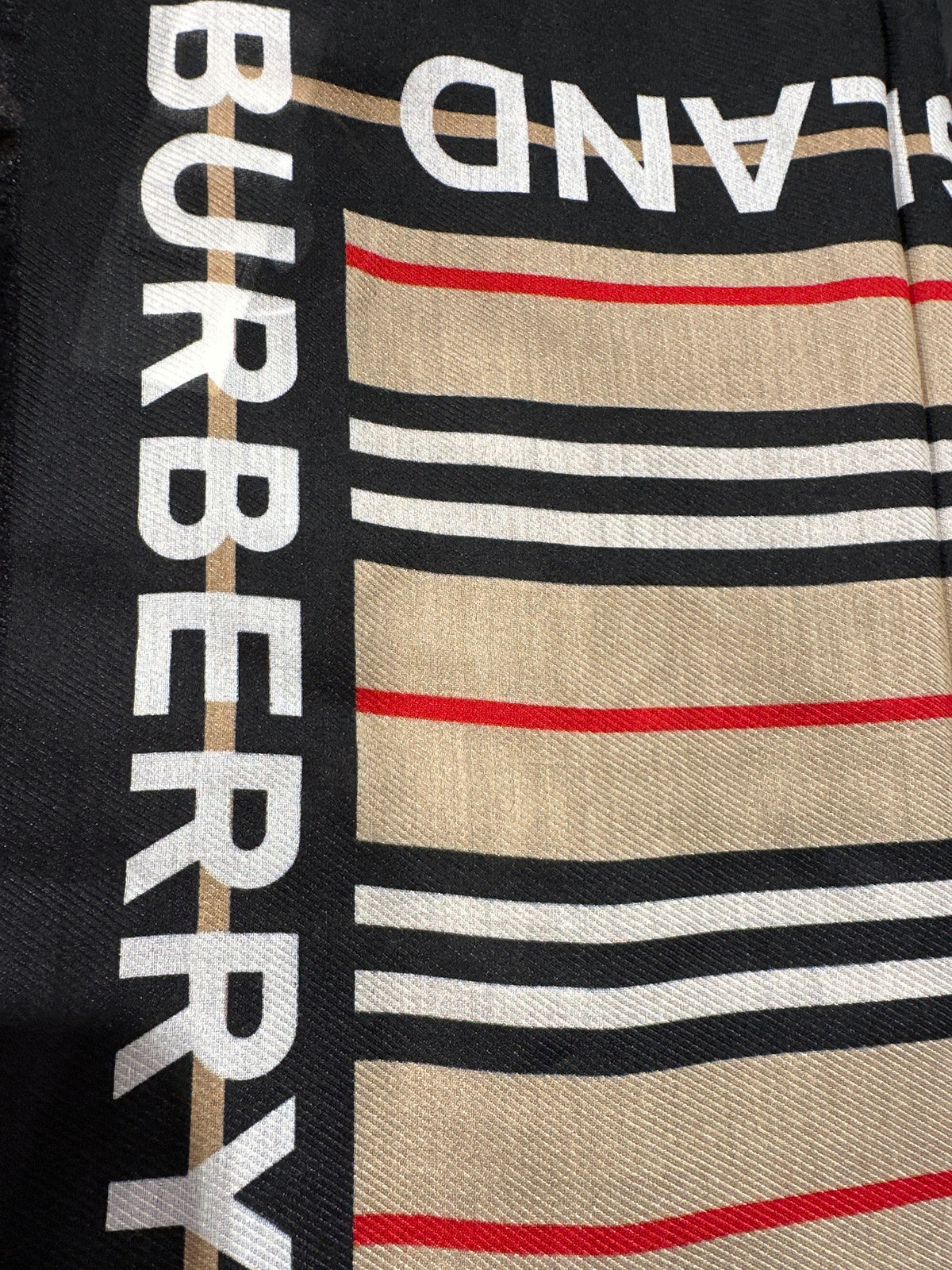 Burberry Tuch, Nahaufnahme des schwarzen Randes mit weißem Schriftzug und beige-roten Streifen